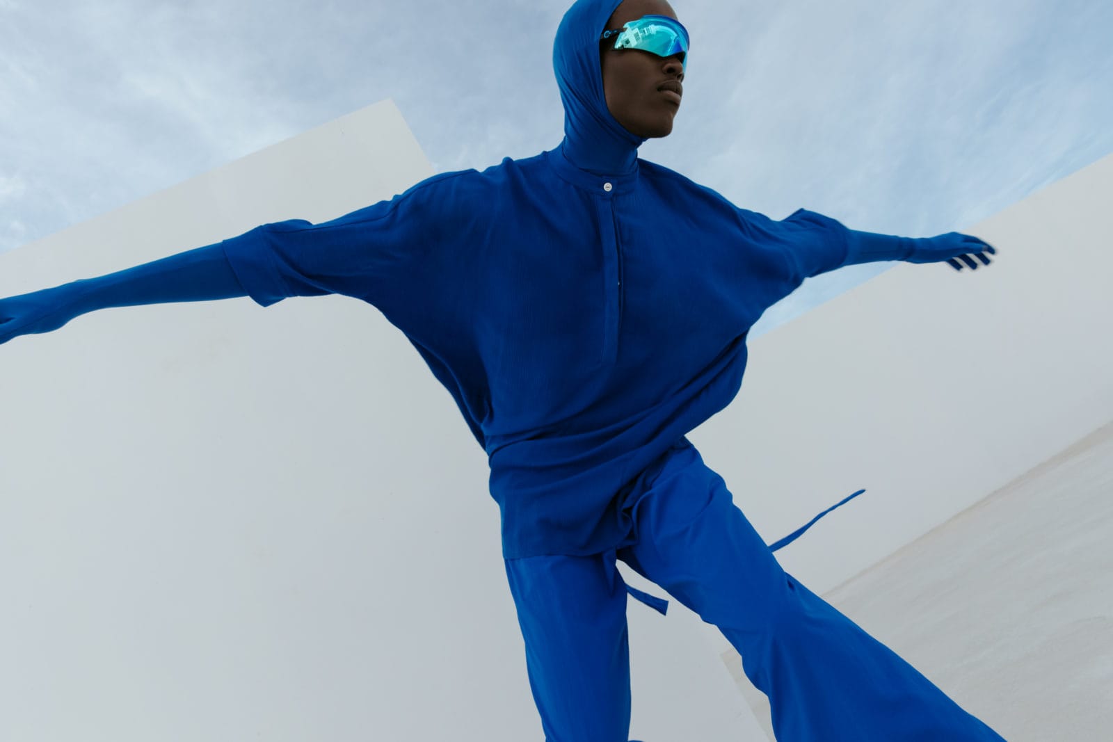 Pivot이 MERWE MODE 상의와 바지, 발라클라바, 장갑을 착용하고 OAKLEY 선글라스를 착용하고 있다.