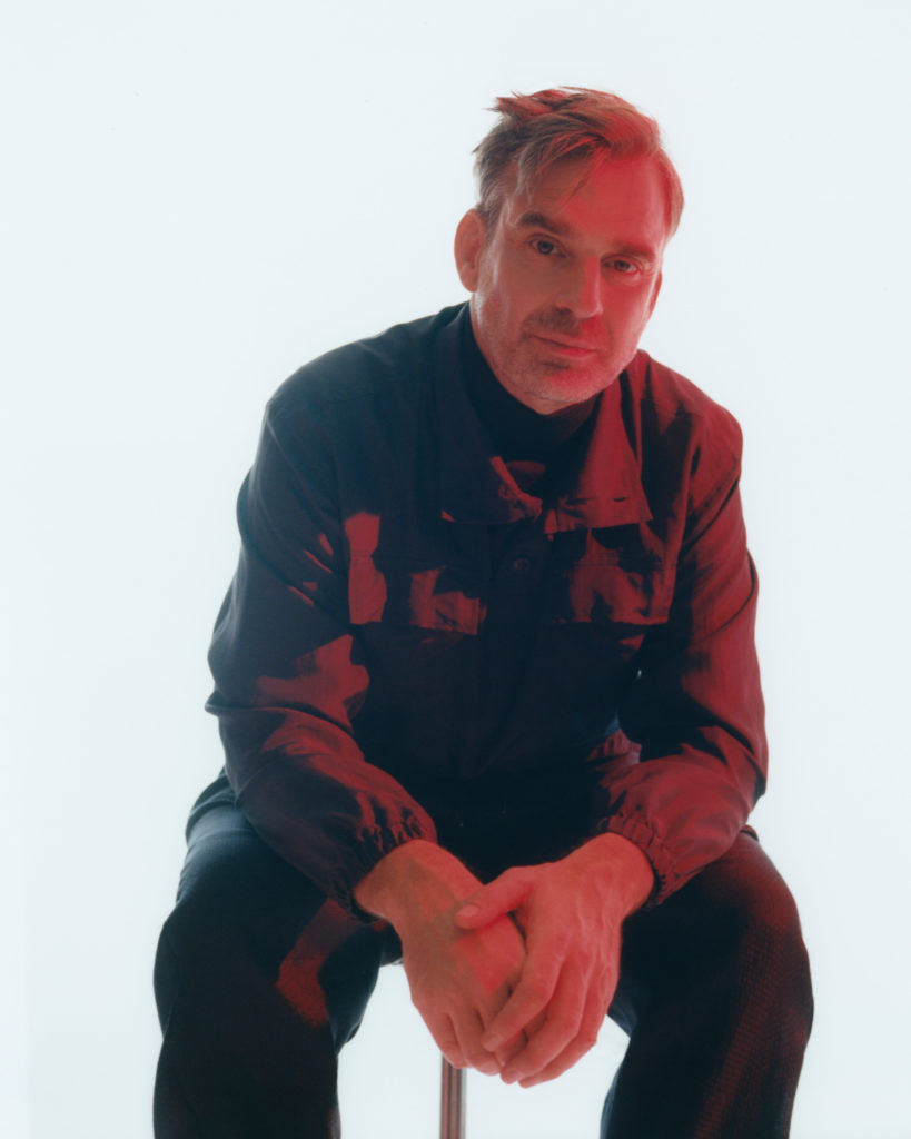 He wears a turtleneck by COS and a shirt and trousers by GIORGIO ARMANI.