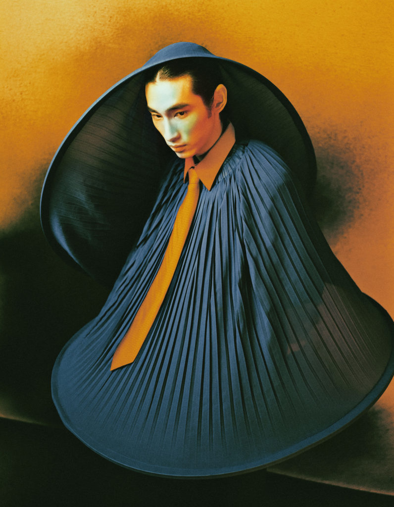 He wears a circular hat and top by TERRENCE ZHOU and a shirt and tie by MARK JEN HSU STUDIO.