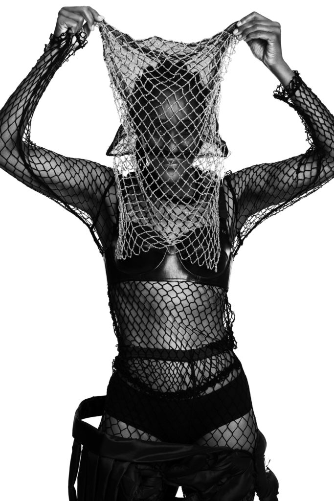 She wears a bra by COMME DES GARÇONS (SS14), a top by COMME DES GARÇONS (SS19) and a headpiece by PIERS ATKINSON.